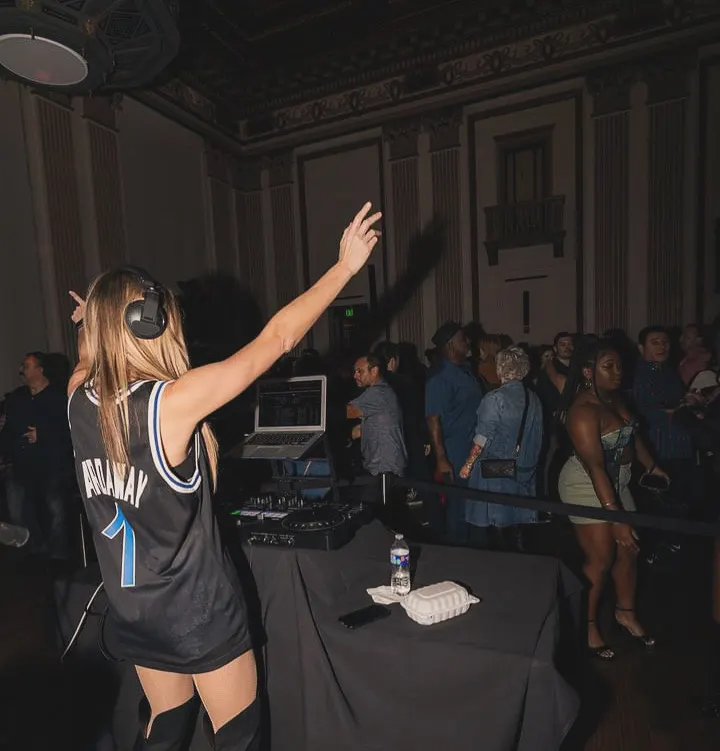 DJ Lyndsay Brown with an arm raised to a crowd in a ballroom